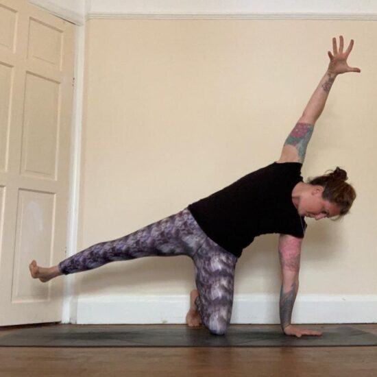 Sarah in a side-plank variation on a dark mat against a cream door