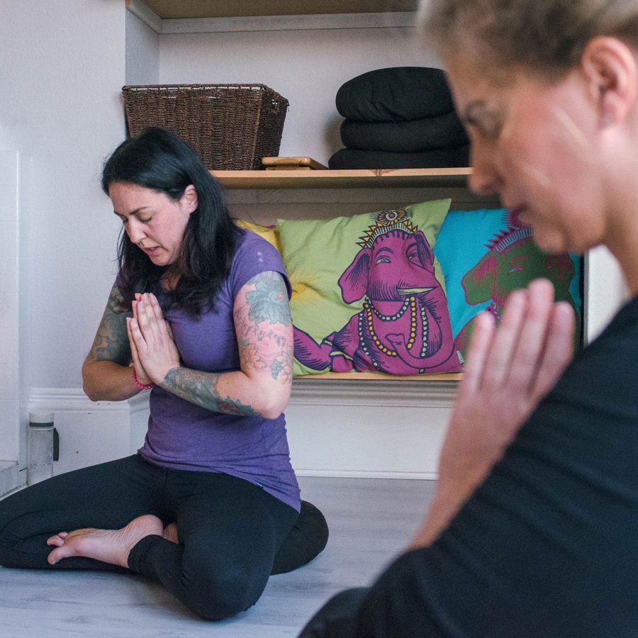 Sarah kneeling with hands together in front of her chest, in her front room
